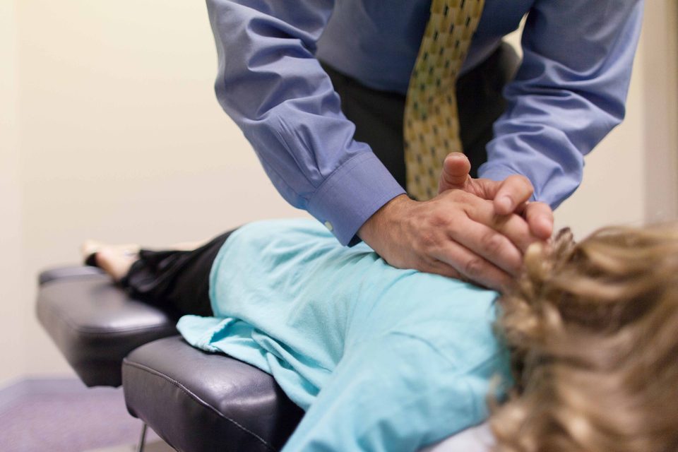 A chiropractor applying a hands-on adjustment to the upper back